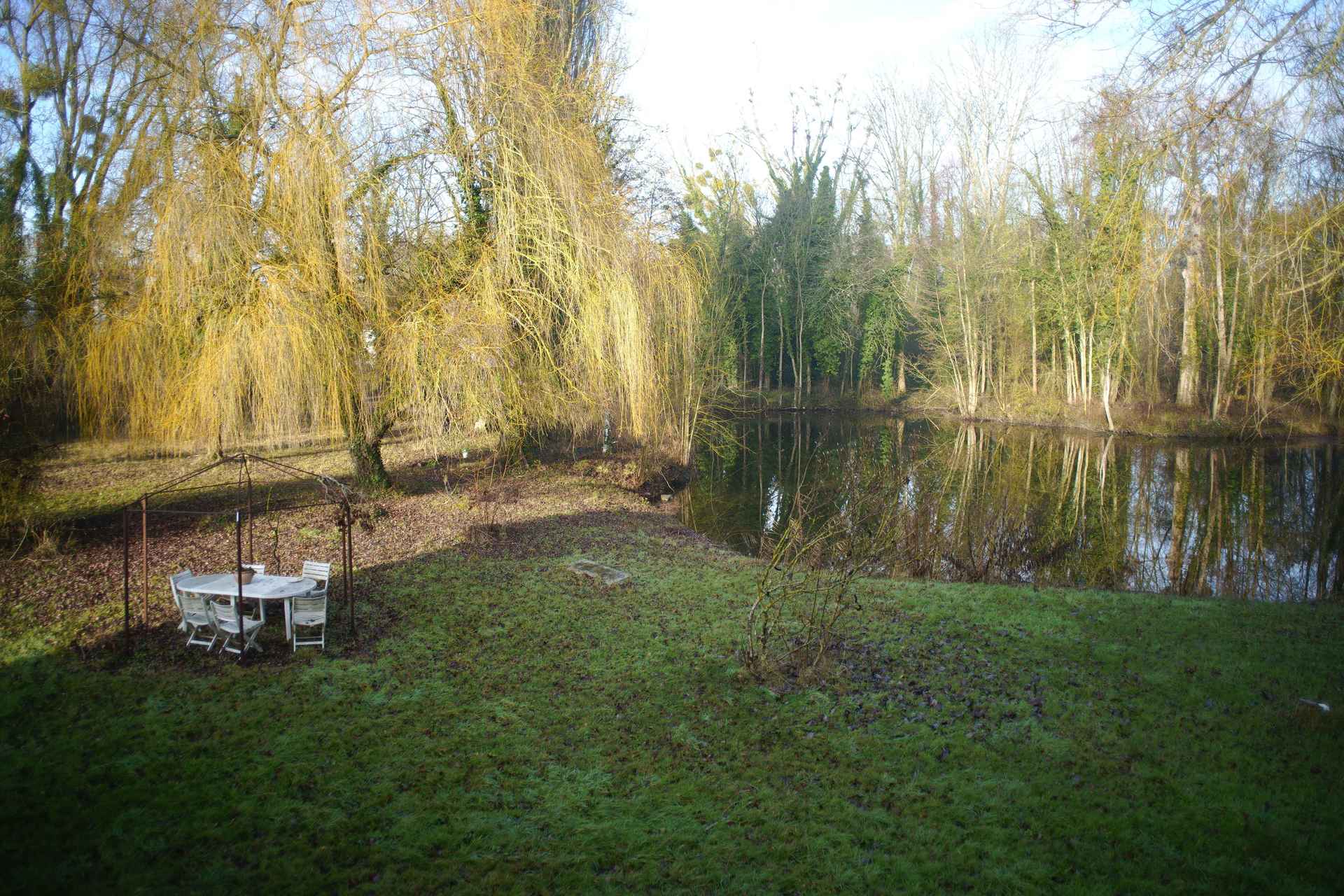 Vue large du jardin avec table au bord de l'étang, idéal pour lendemain de mariage